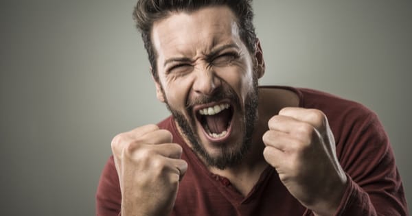 A man screaming in anger in a red shirt with a grey background