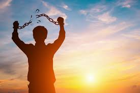 A silhouette of a person with their arms in the air breaking a chain tied to them in half