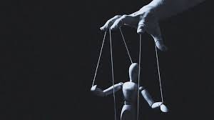 A figure of a person attached to strings being controlled by a hand above with a black background