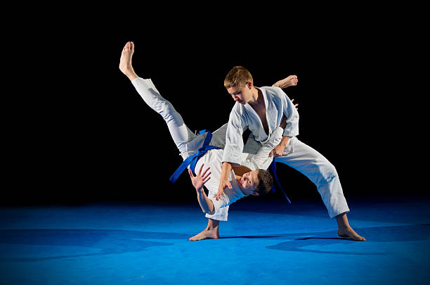 A fighter in a uniform taking down another martial artist hitting the blue mat
