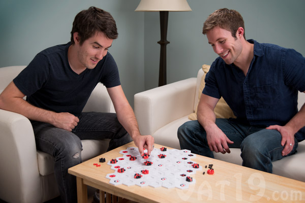 Two smiling guys sitting down playing a board game on a table